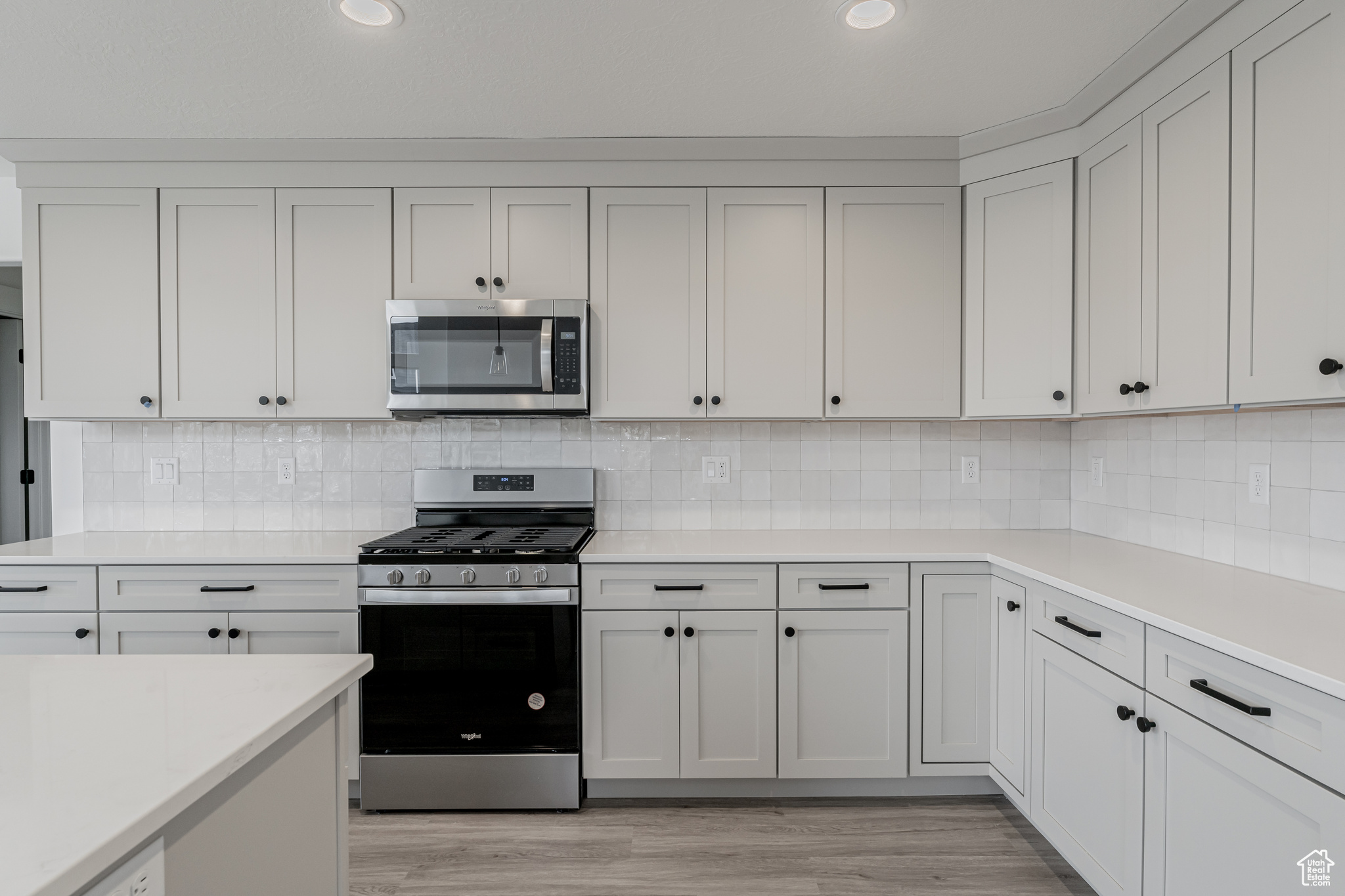 Kitchen featuring appliances with stainless steel finishes, light wood-type flooring, backsplash, and white cabinetry