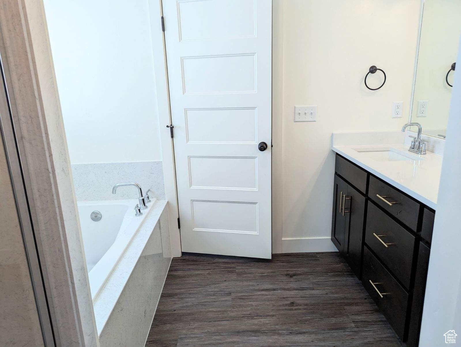 Bathroom with hardwood / wood-style flooring, tiled bath, and vanity