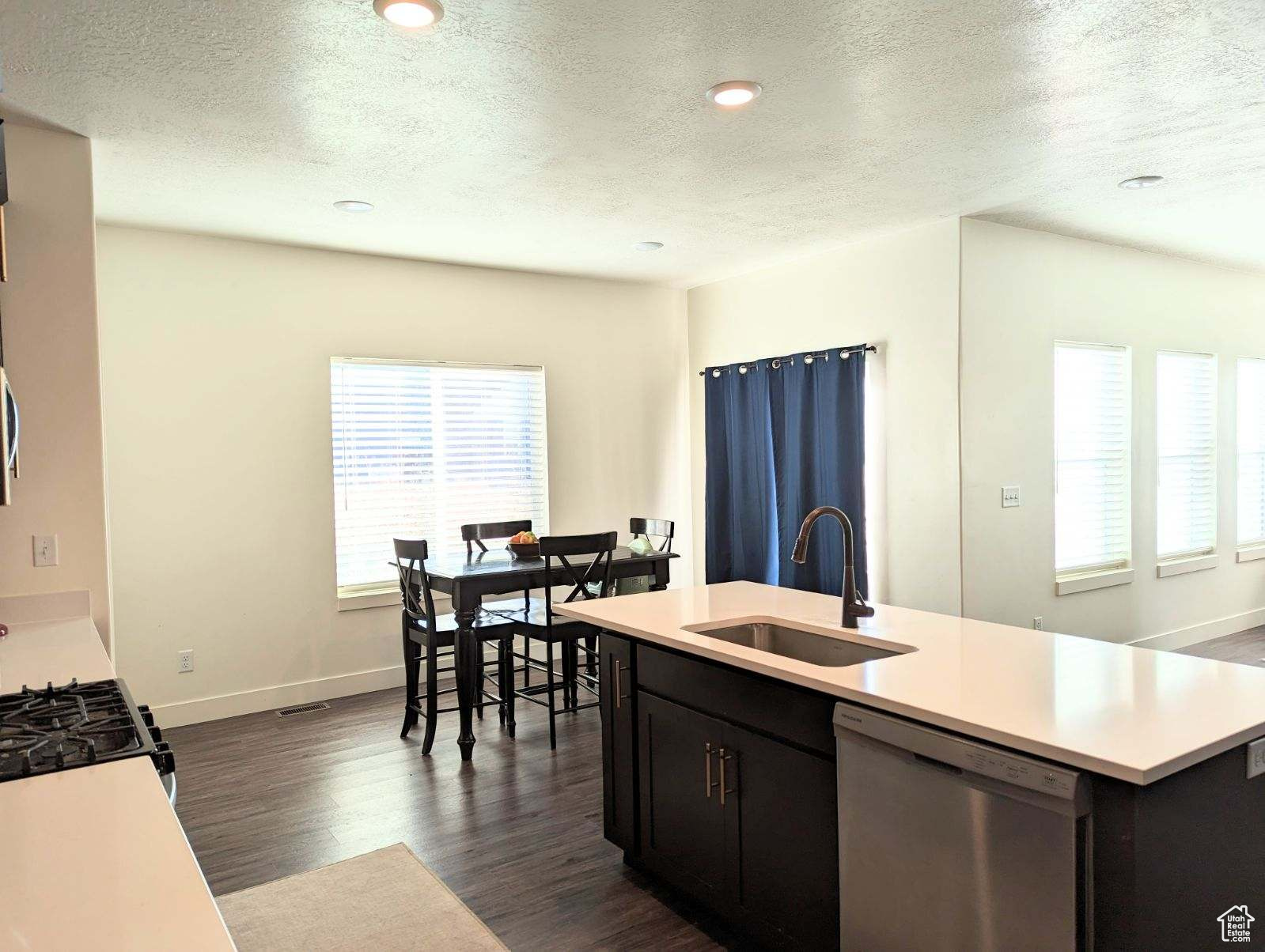 Kitchen with an island with sink, dishwasher, dark wood-type flooring, a textured ceiling, and sink