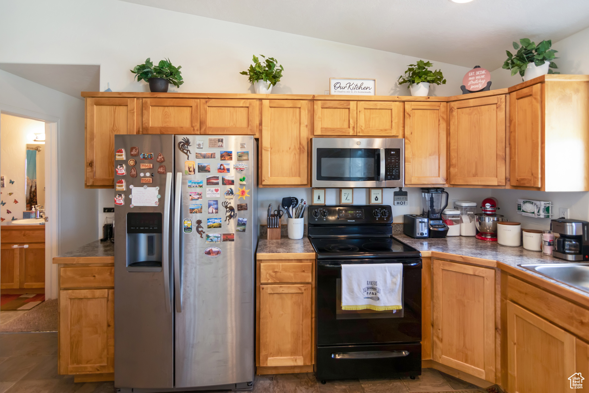 Kitchen with stainless steel appliances, sink, tile floors, and lofted ceiling