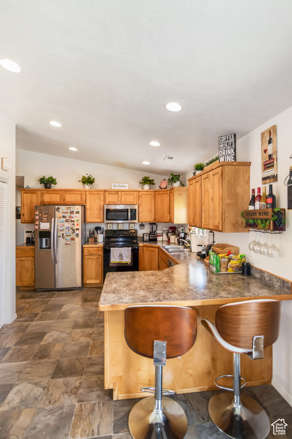 Kitchen with appliances with stainless steel finishes, lofted ceiling, dark tile flooring, and kitchen peninsula