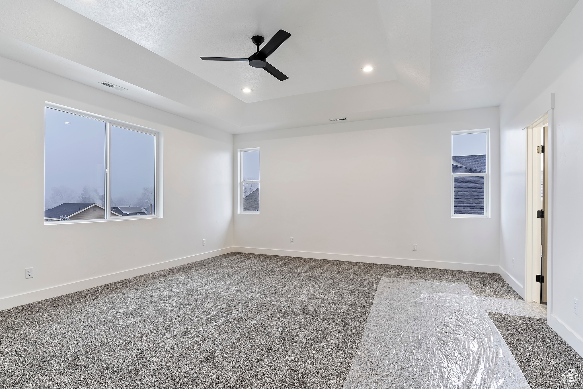 Empty room with a raised ceiling, carpet, and ceiling fan