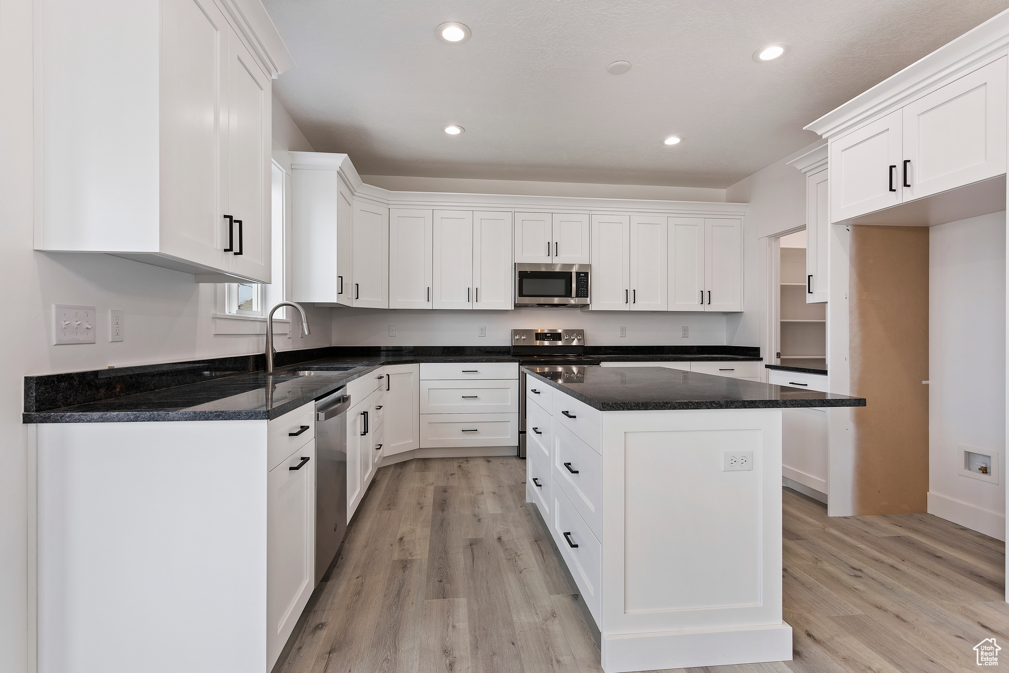 Kitchen with a center island, light wood-type flooring, stainless steel appliances, white cabinets, and sink