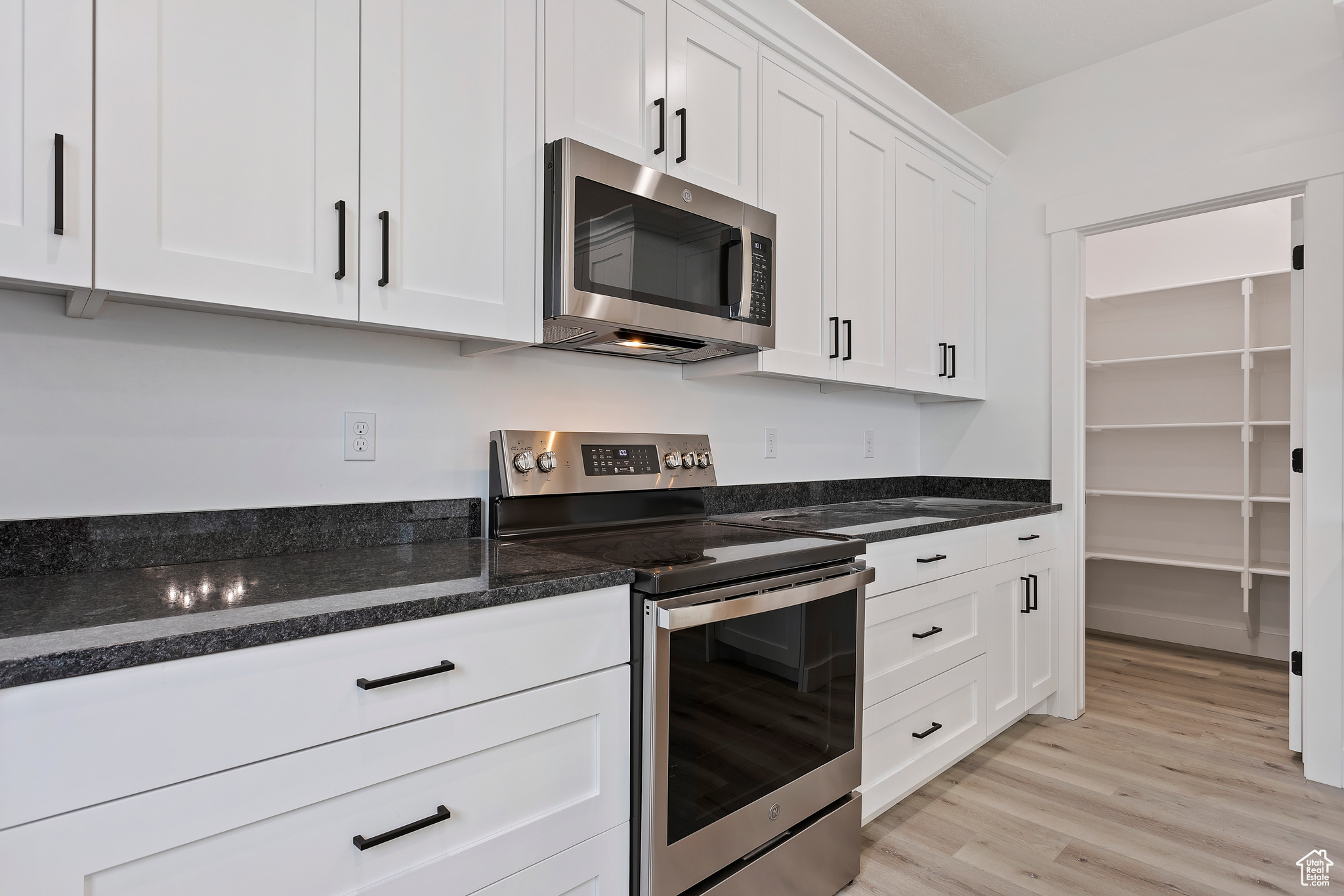 Kitchen with white cabinetry, dark stone countertops, light hardwood / wood-style flooring, and stainless steel appliances