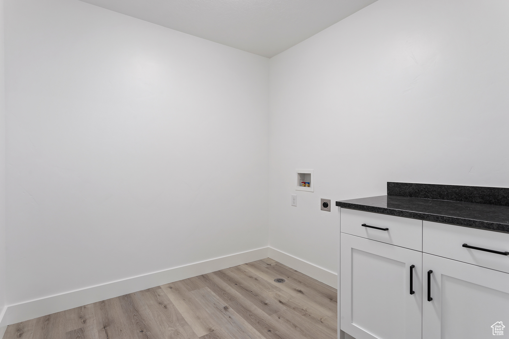 Clothes washing area with light hardwood / wood-style floors, hookup for an electric dryer, hookup for a washing machine, and cabinets