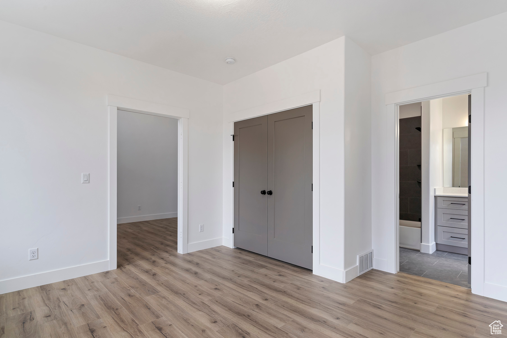 Unfurnished bedroom with a closet, ensuite bathroom, and light wood-type flooring