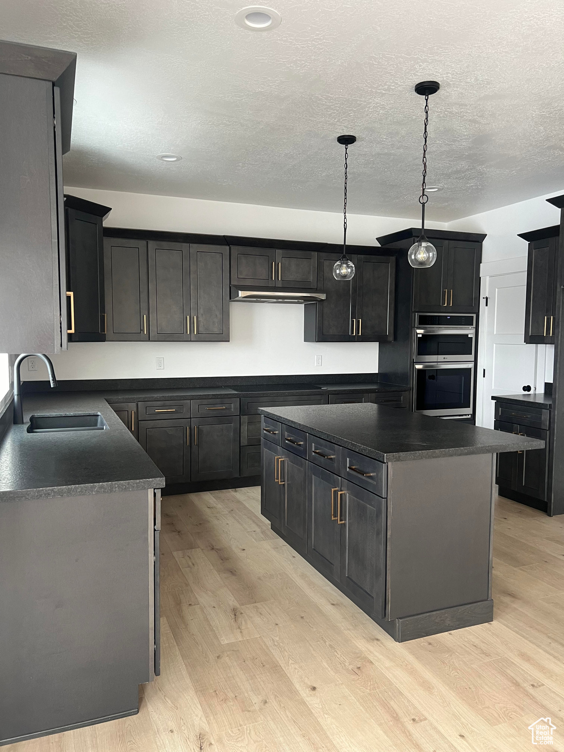 Kitchen featuring a kitchen island, sink, stainless steel double oven, and light wood-type flooring