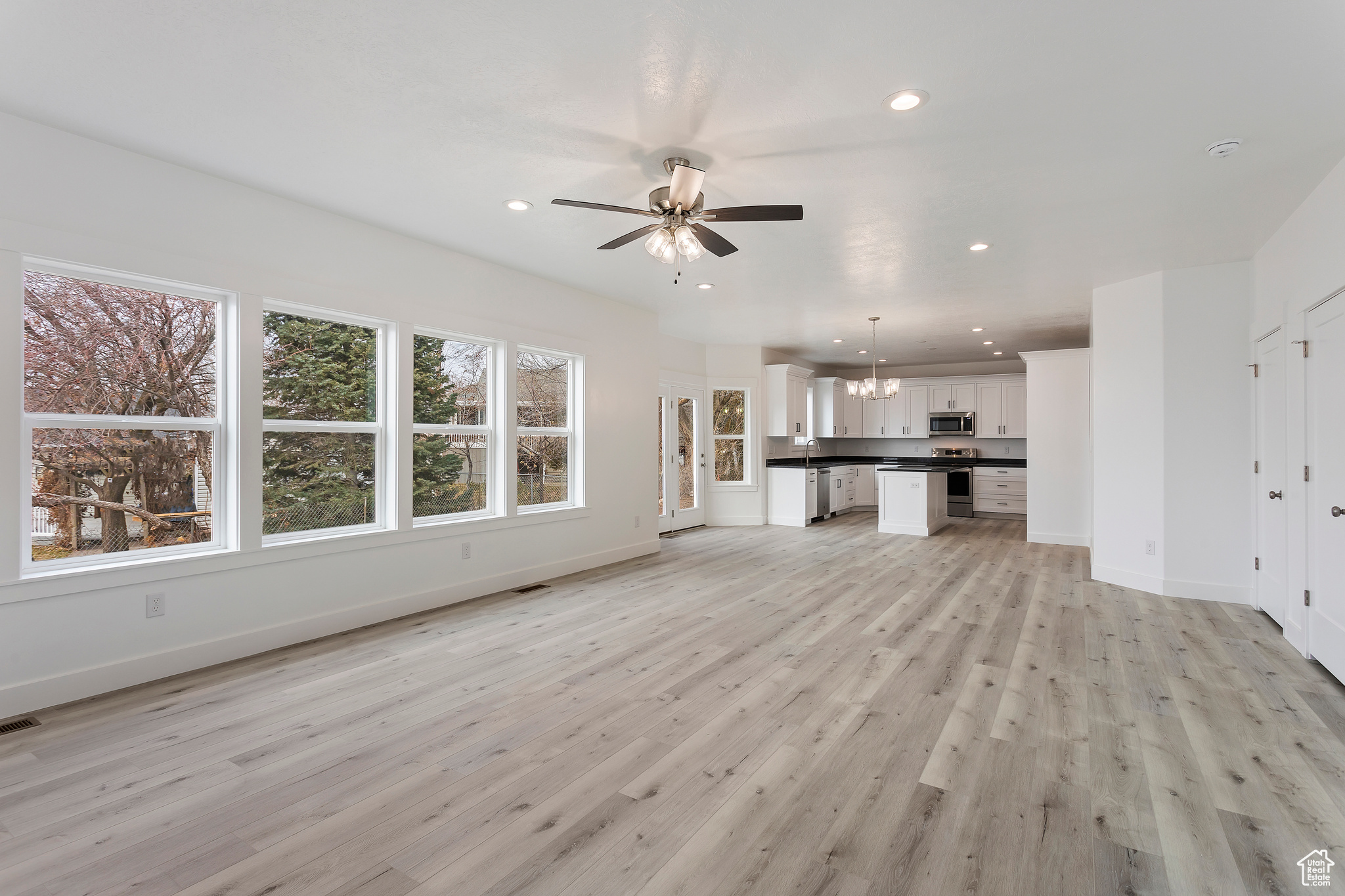 Unfurnished living room featuring light wood-type flooring and ceiling fan with notable chandelier