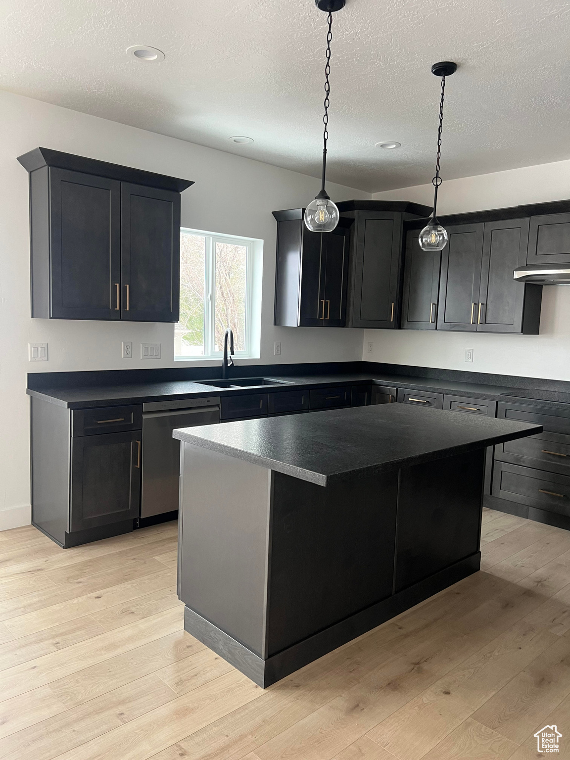 Kitchen featuring a kitchen island, dishwasher, light wood-type flooring, sink, and a textured ceiling