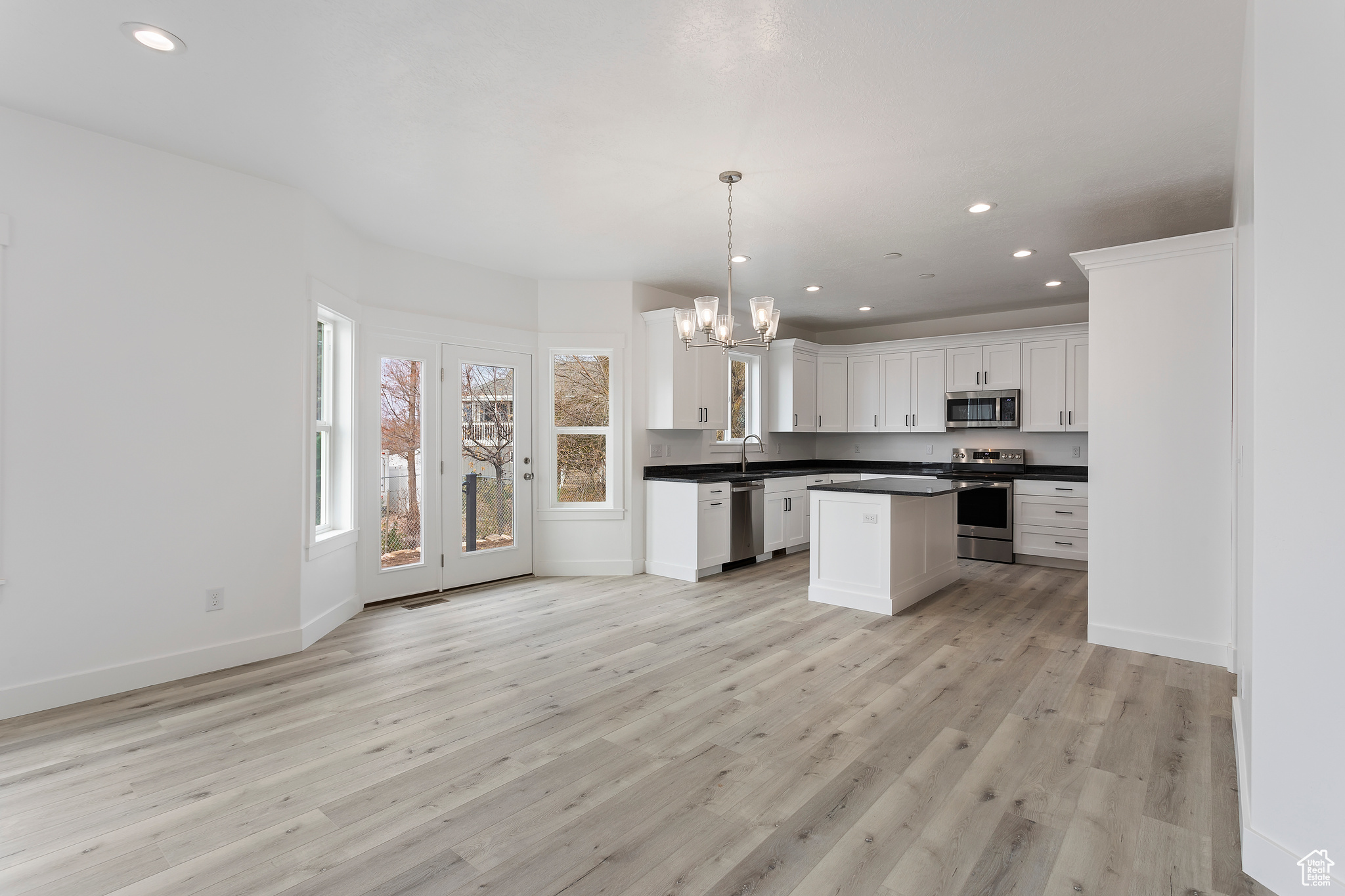 Kitchen with white cabinetry, light hardwood / wood-style flooring, appliances with stainless steel finishes, decorative light fixtures, and sink