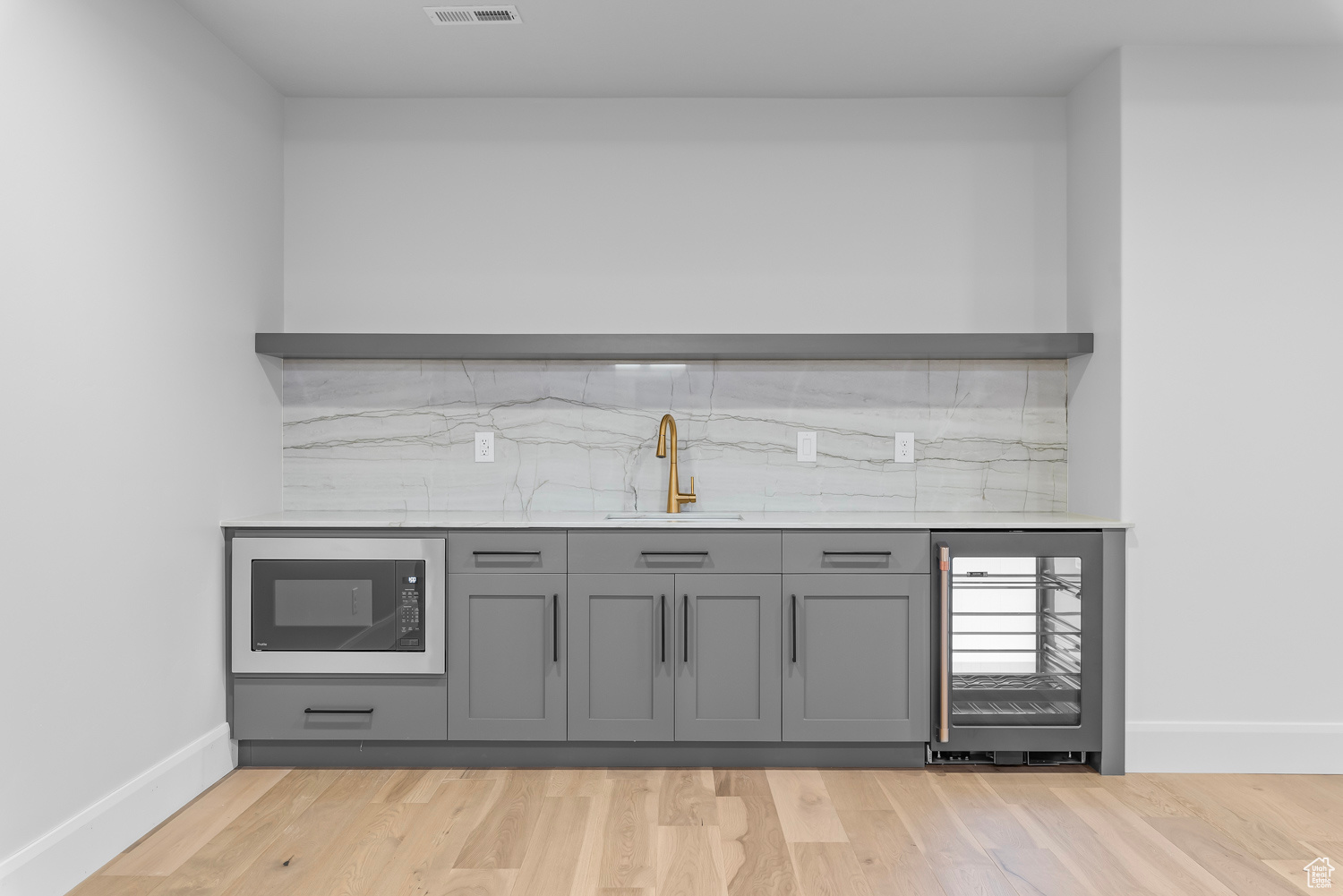 Bar featuring light wood-type flooring, tasteful backsplash, black microwave, wine cooler, and sink