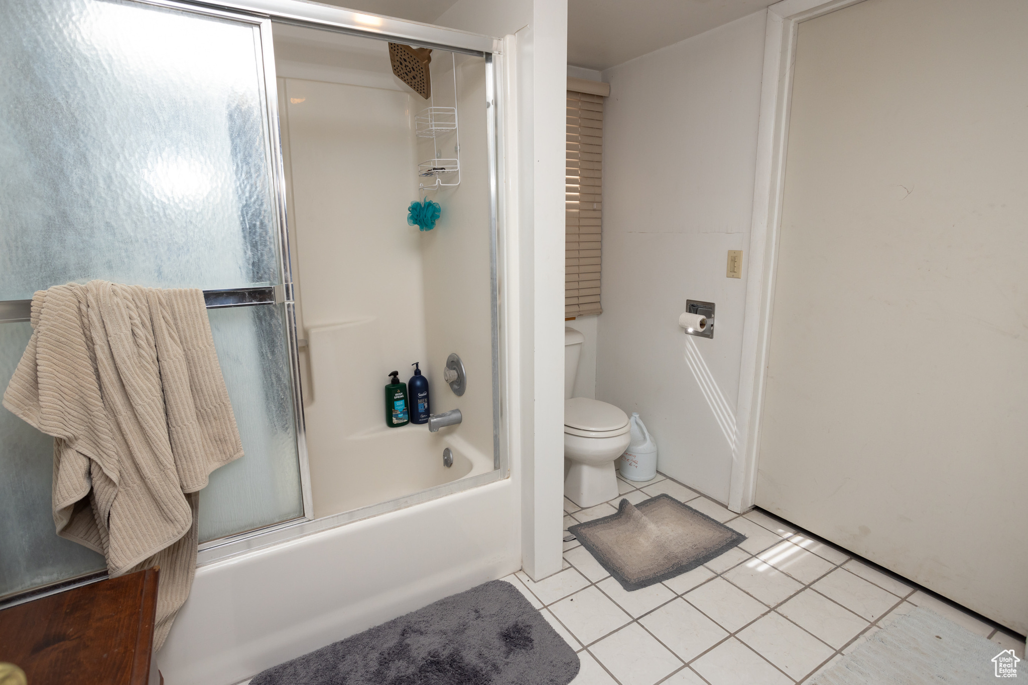 Bathroom featuring tile flooring, combined bath / shower with glass door, and toilet