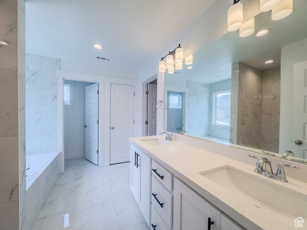 Bathroom featuring a relaxing tiled tub, dual vanity, and tile patterned floors