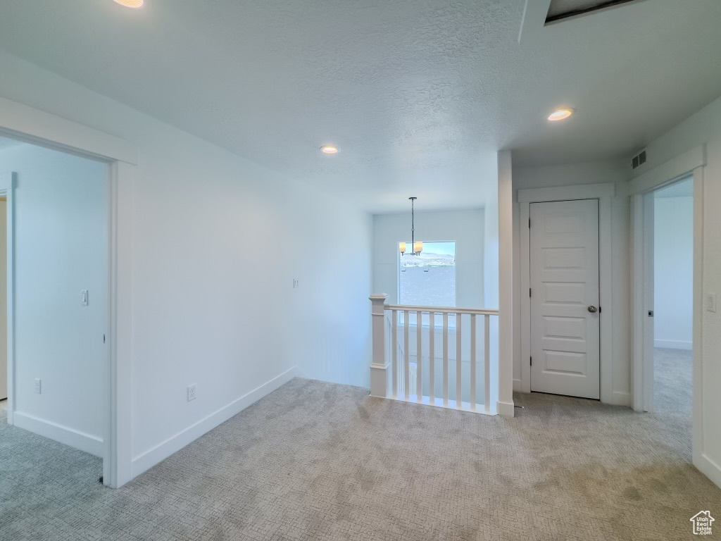 Carpeted empty room with a textured ceiling and an inviting chandelier