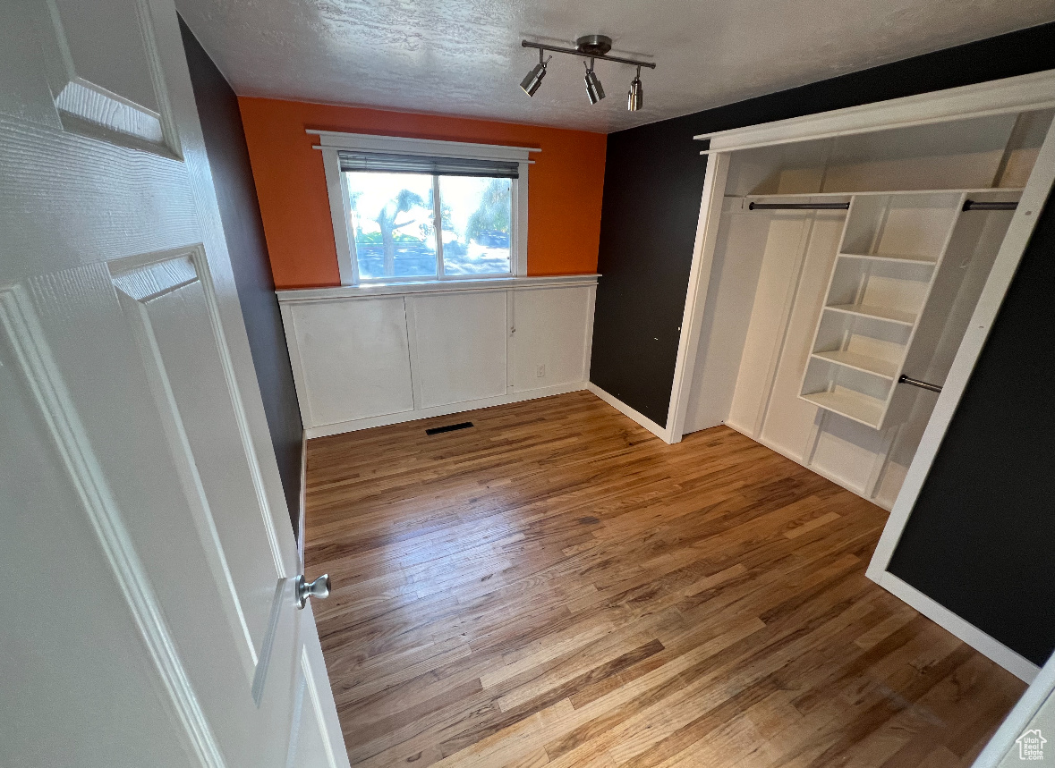 Spare room featuring light wood-type flooring, track lighting, and a textured ceiling