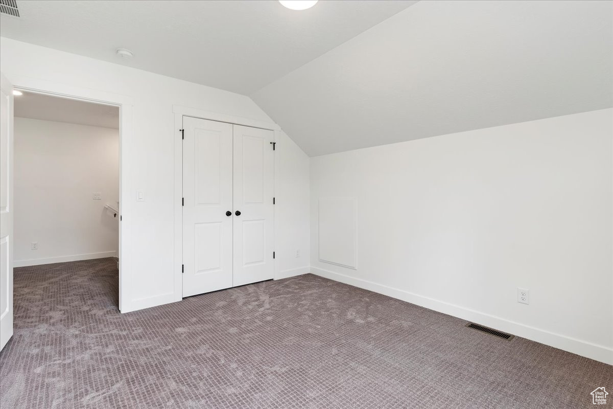 Additional living space with dark colored carpet and vaulted ceiling