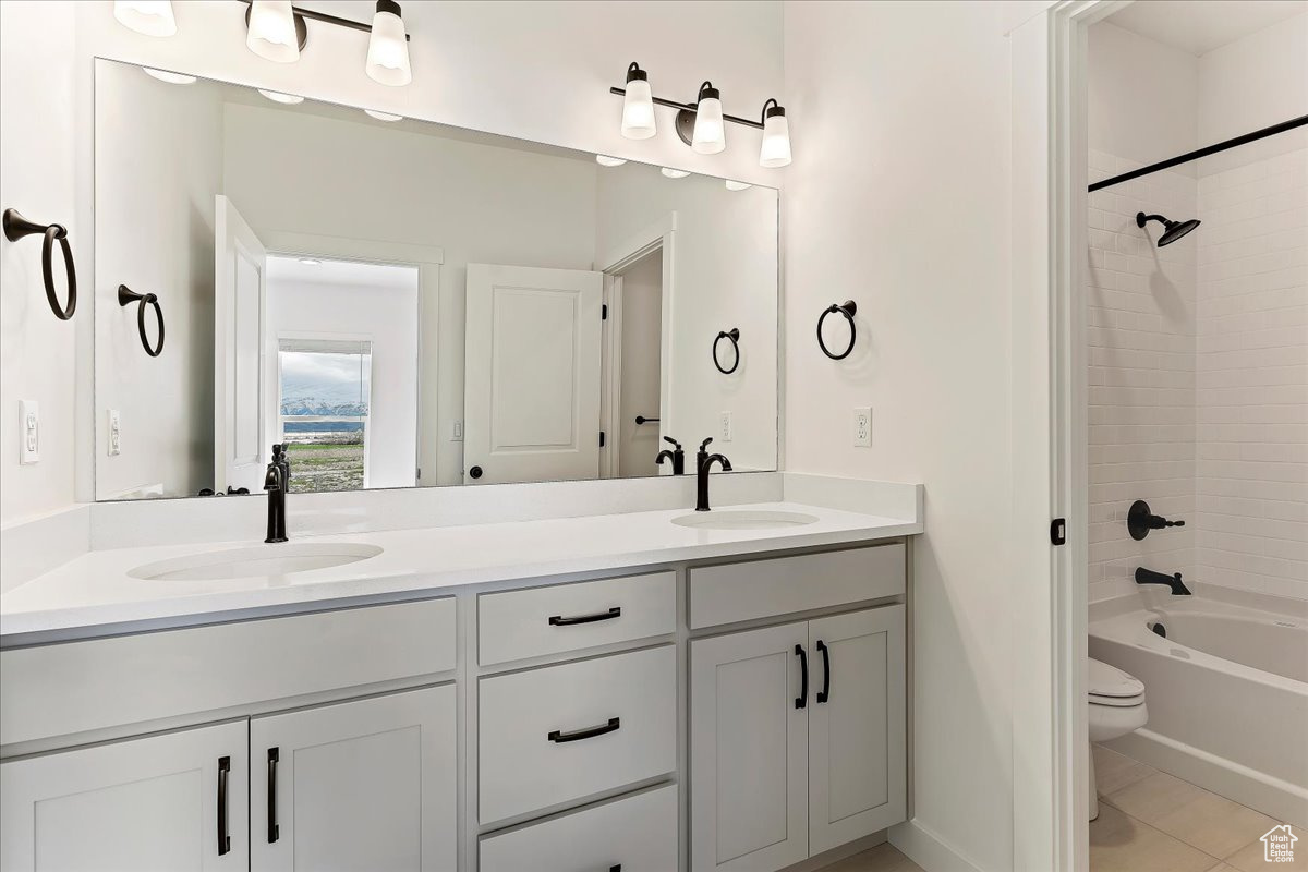 Full bathroom featuring tiled shower / bath, double sink vanity, tile flooring, and toilet