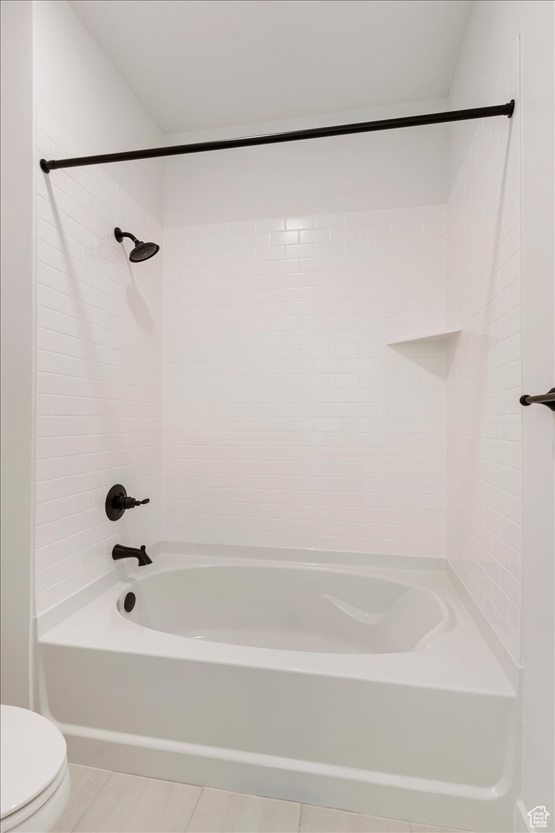 Bathroom featuring tiled shower / bath, tile flooring, and toilet