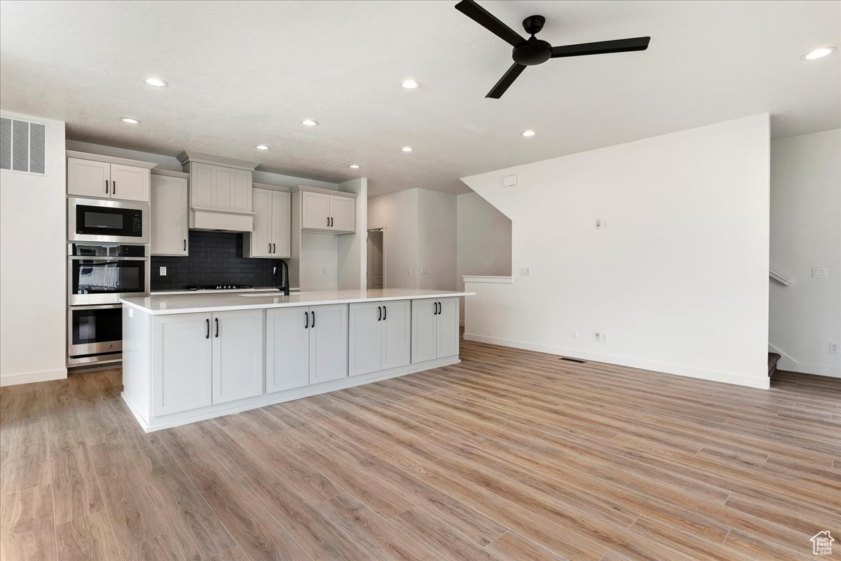 Kitchen featuring a center island with sink, built in microwave, and light wood-type flooring