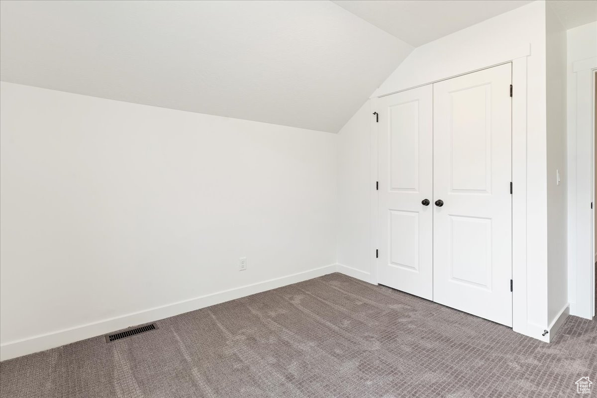 Additional living space with lofted ceiling and dark colored carpet