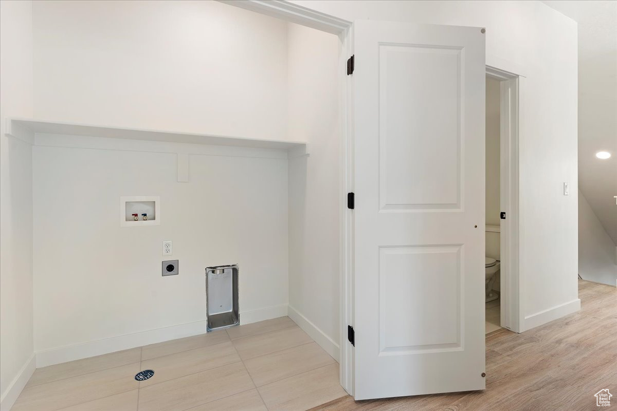 Laundry area with hookup for an electric dryer, light wood-type flooring, and washer hookup