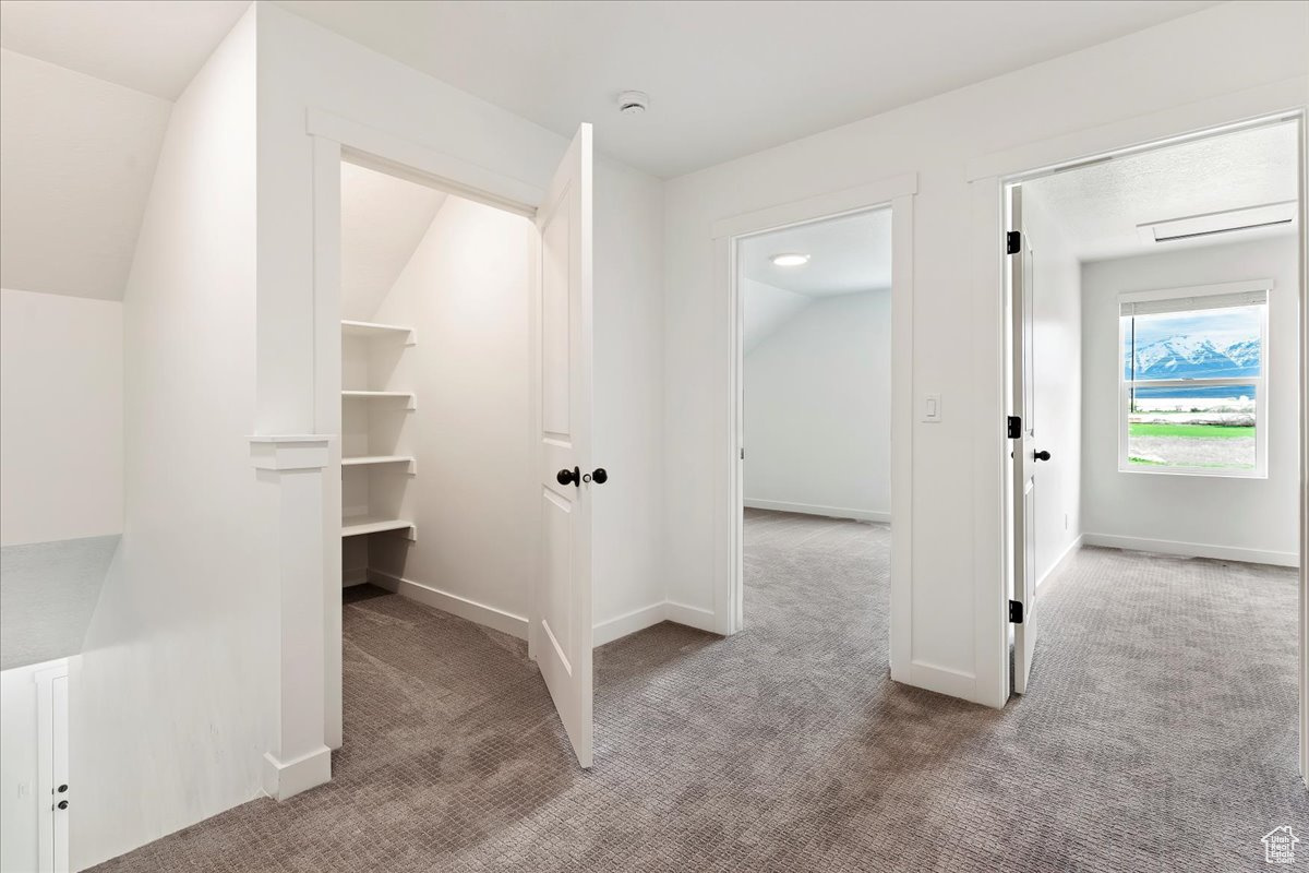 Corridor with dark colored carpet and lofted ceiling