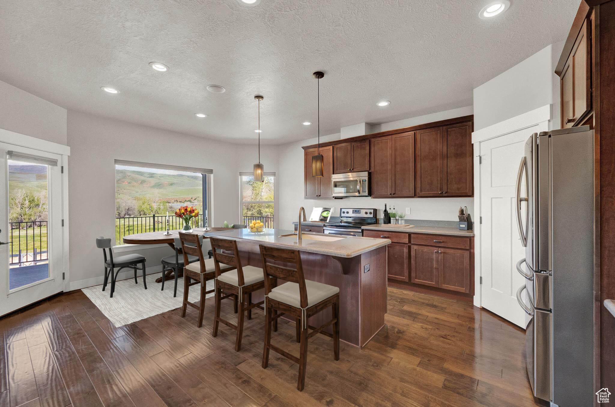 Kitchen featuring dark hardwood / wood-style flooring, stainless steel appliances, a kitchen island with sink, pendant lighting, and sink