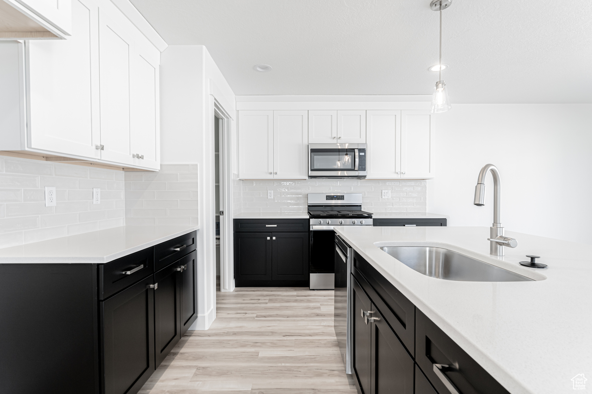 Kitchen featuring sink, white cabinetry, hanging light fixtures, light hardwood / wood-style flooring, and appliances with stainless steel finishes