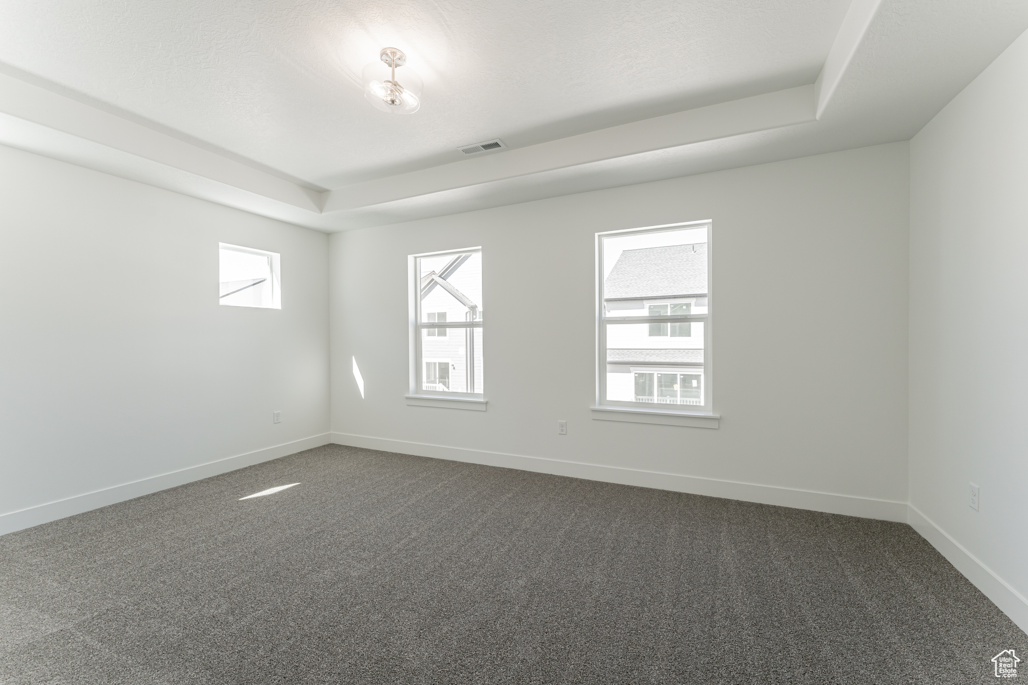 Empty room with a tray ceiling, dark colored carpet, and a wealth of natural light