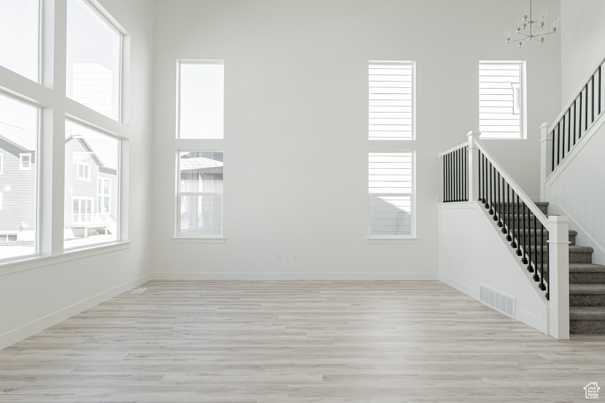 Unfurnished living room with a towering ceiling, light hardwood / wood-style floors, and a chandelier