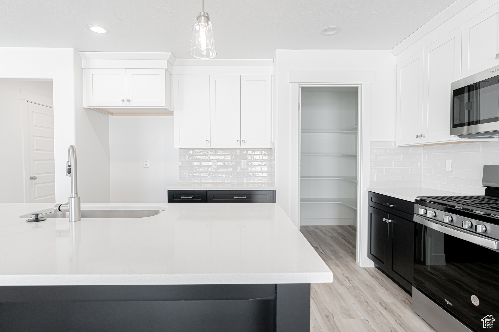 Kitchen with sink, tasteful backsplash, decorative light fixtures, white cabinetry, and stainless steel appliances