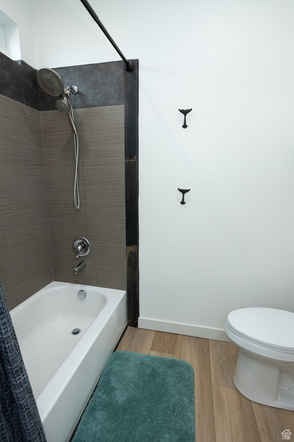 Bathroom with tiled shower / bath combo, wood-type flooring, and toilet