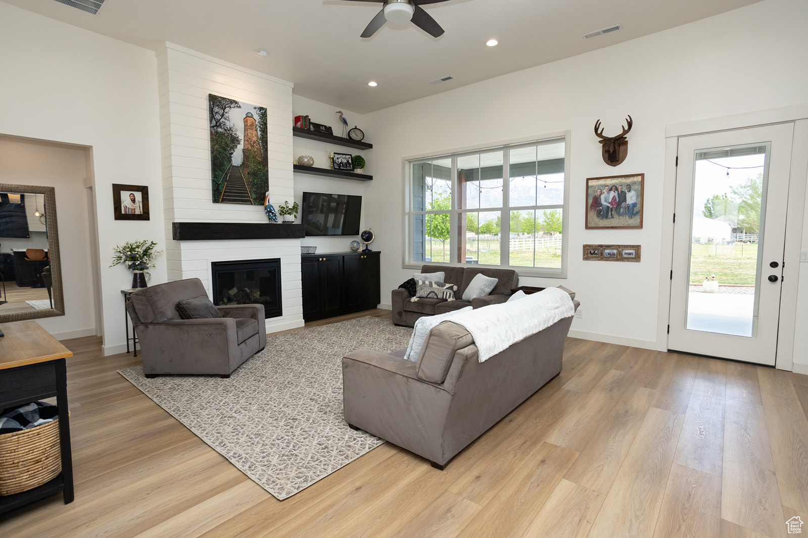 Living room with brick wall, a fireplace, ceiling fan, and light hardwood / wood-style flooring