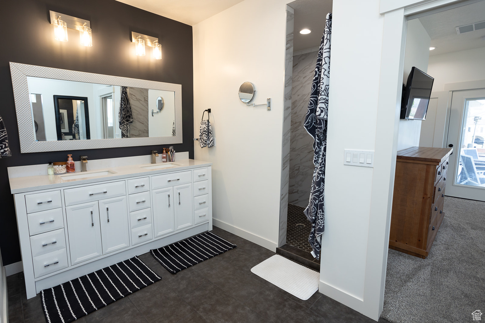 Bathroom featuring tiled shower, dual vanity, and tile floors