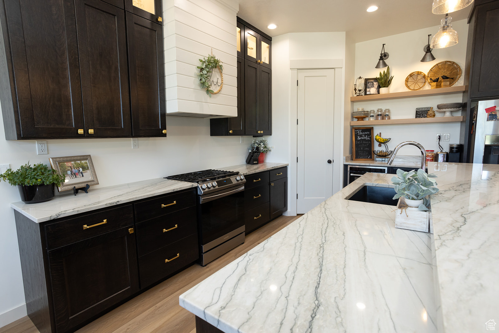 Kitchen with light stone countertops, light hardwood / wood-style flooring, stainless steel range with gas stovetop, custom exhaust hood, and sink