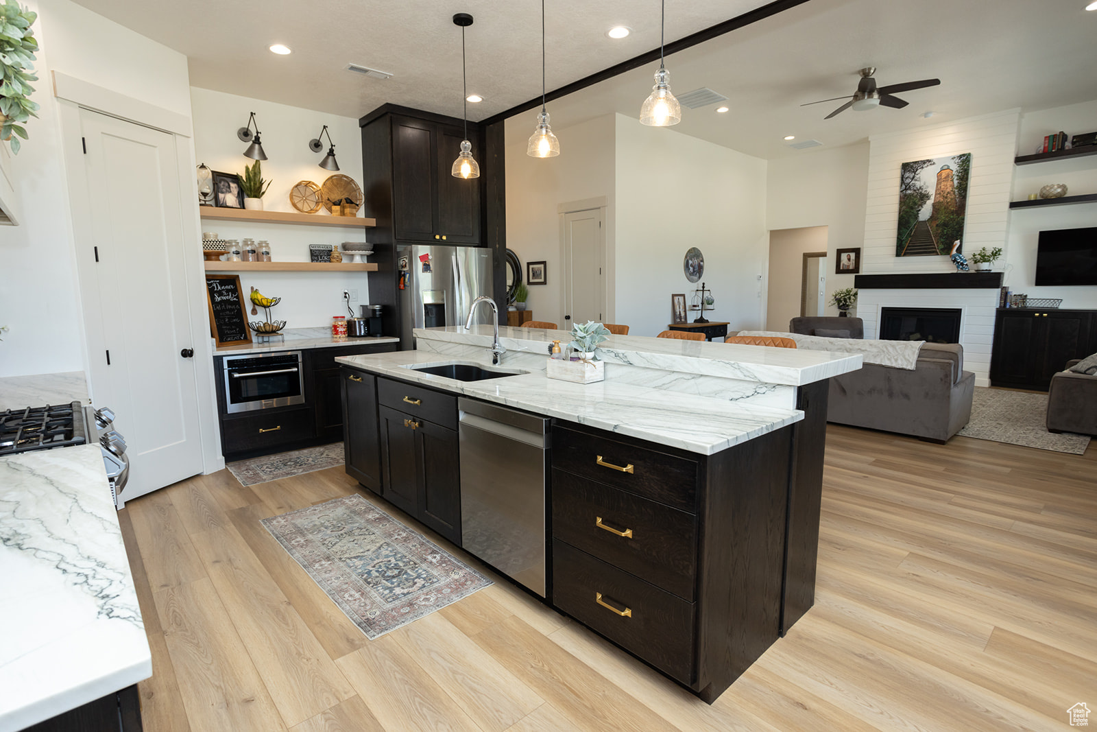 Kitchen with a brick fireplace, a center island with sink, light wood-type flooring, and appliances with stainless steel finishes