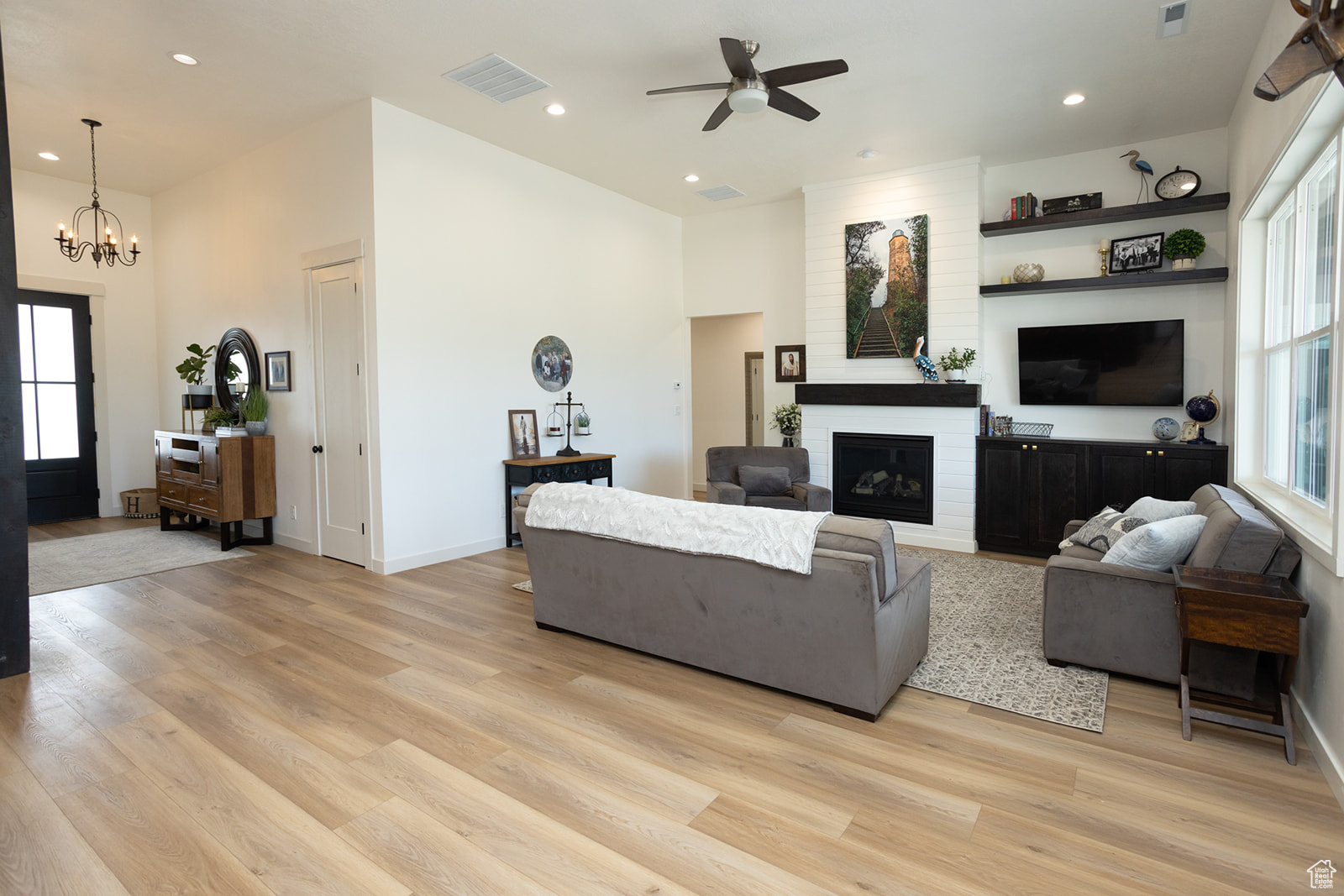 Living room featuring brick wall, a fireplace, light wood-type flooring, and ceiling fan with notable chandelier