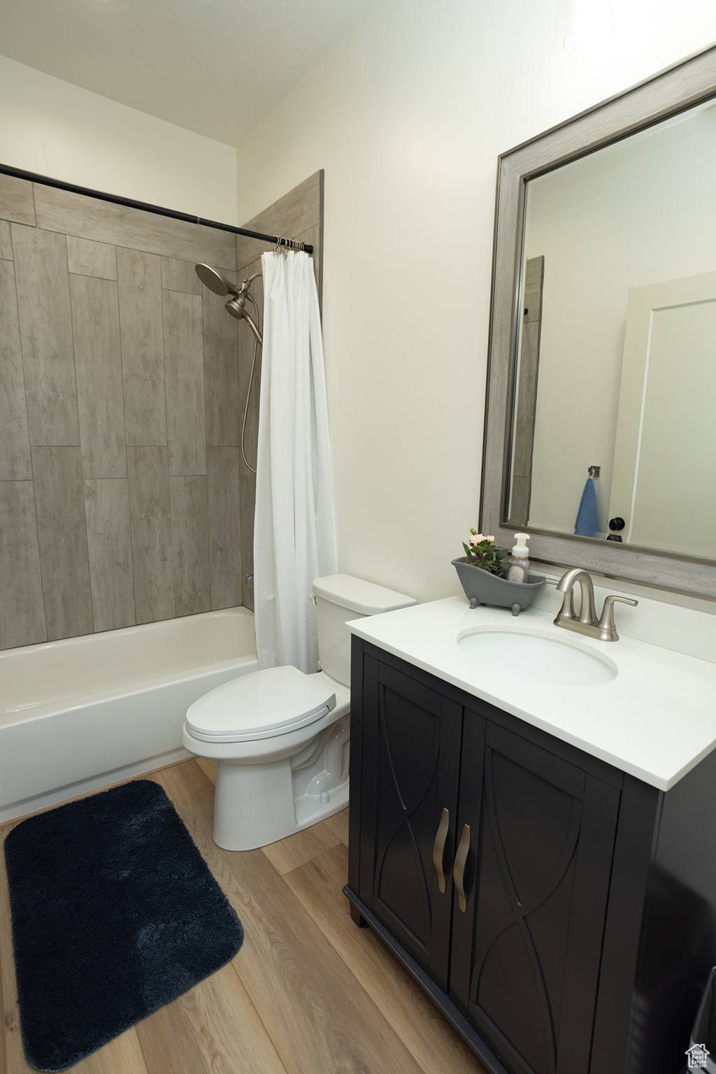 Full bathroom with vanity with extensive cabinet space, toilet, shower / bath combo with shower curtain, and wood-type flooring