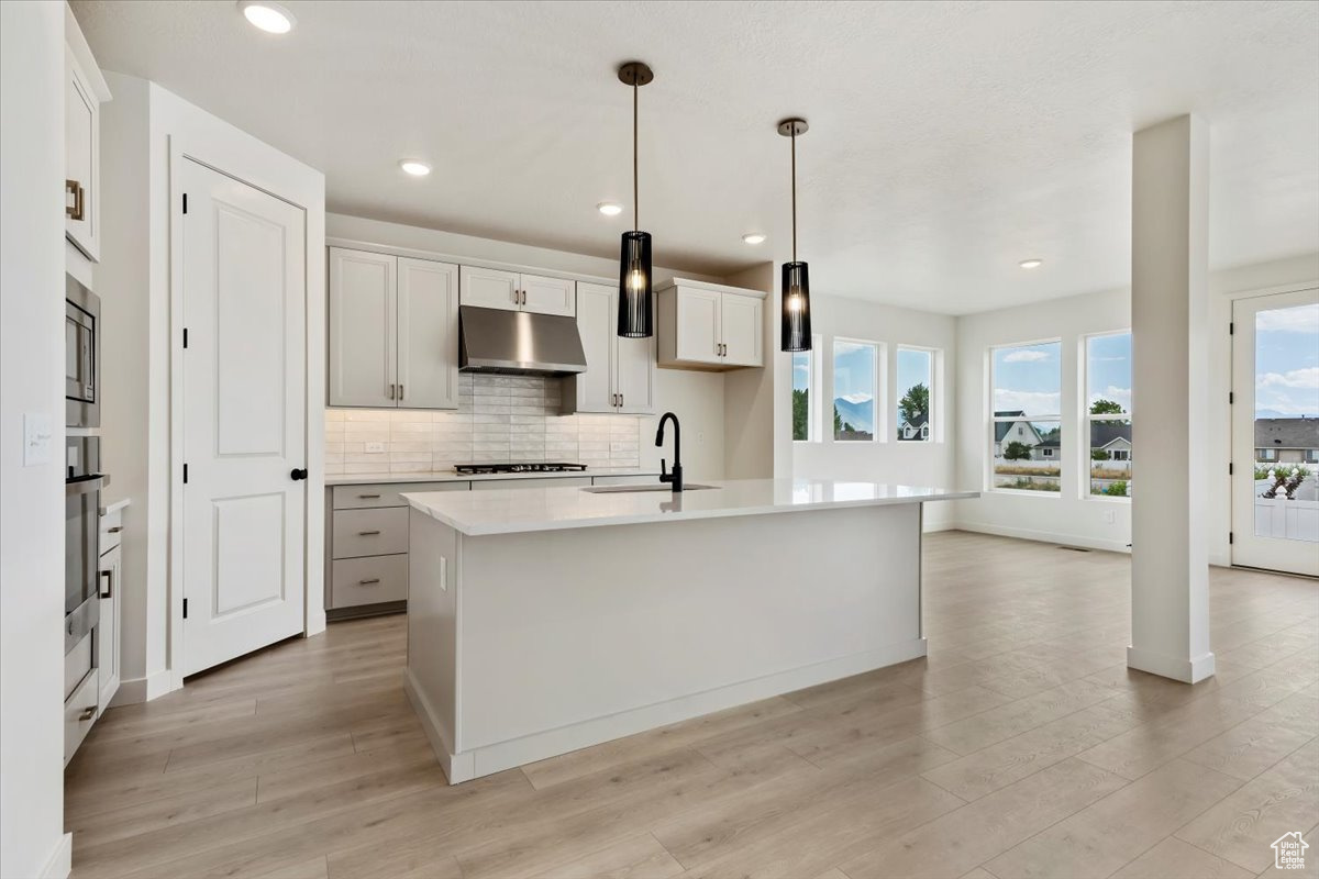 Kitchen featuring white cabinetry, backsplash, a kitchen island with sink, pendant lighting, and sink