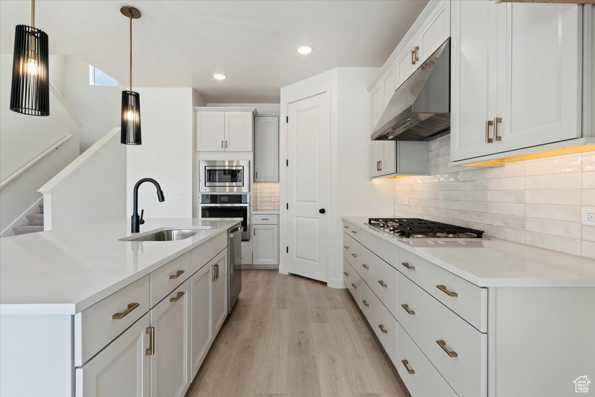 Kitchen with appliances with stainless steel finishes, light hardwood / wood-style flooring, tasteful backsplash, sink, and white cabinetry