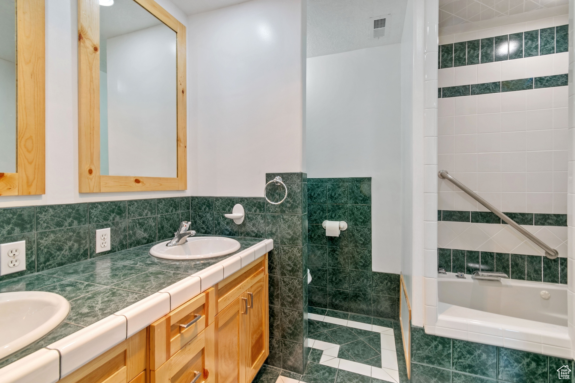 Bathroom with tile walls, tile flooring, vanity with extensive cabinet space, and dual sinks