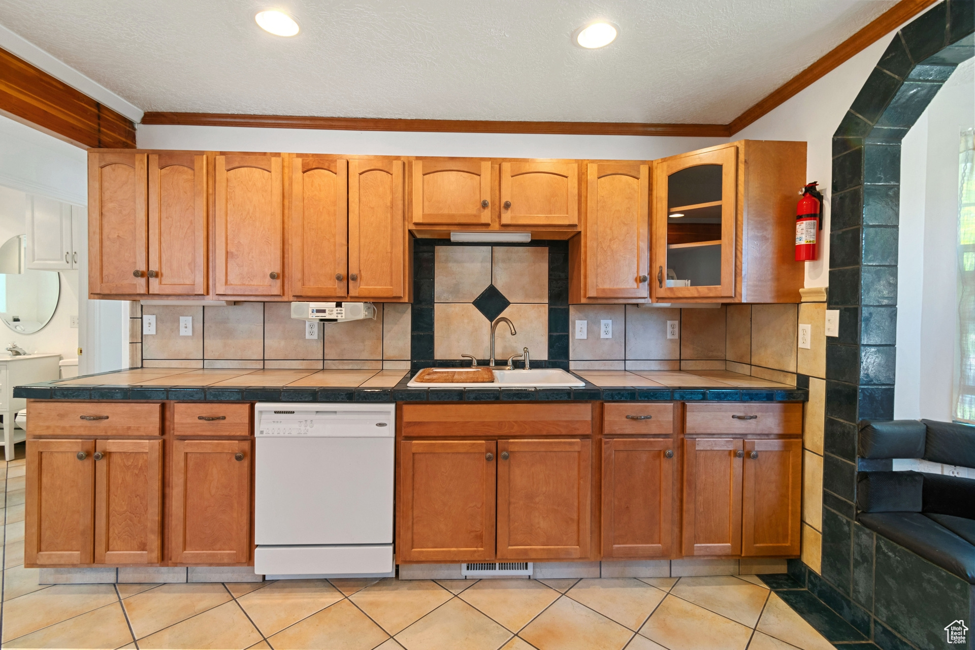 Kitchen with sink, dishwasher, crown molding, and light tile flooring