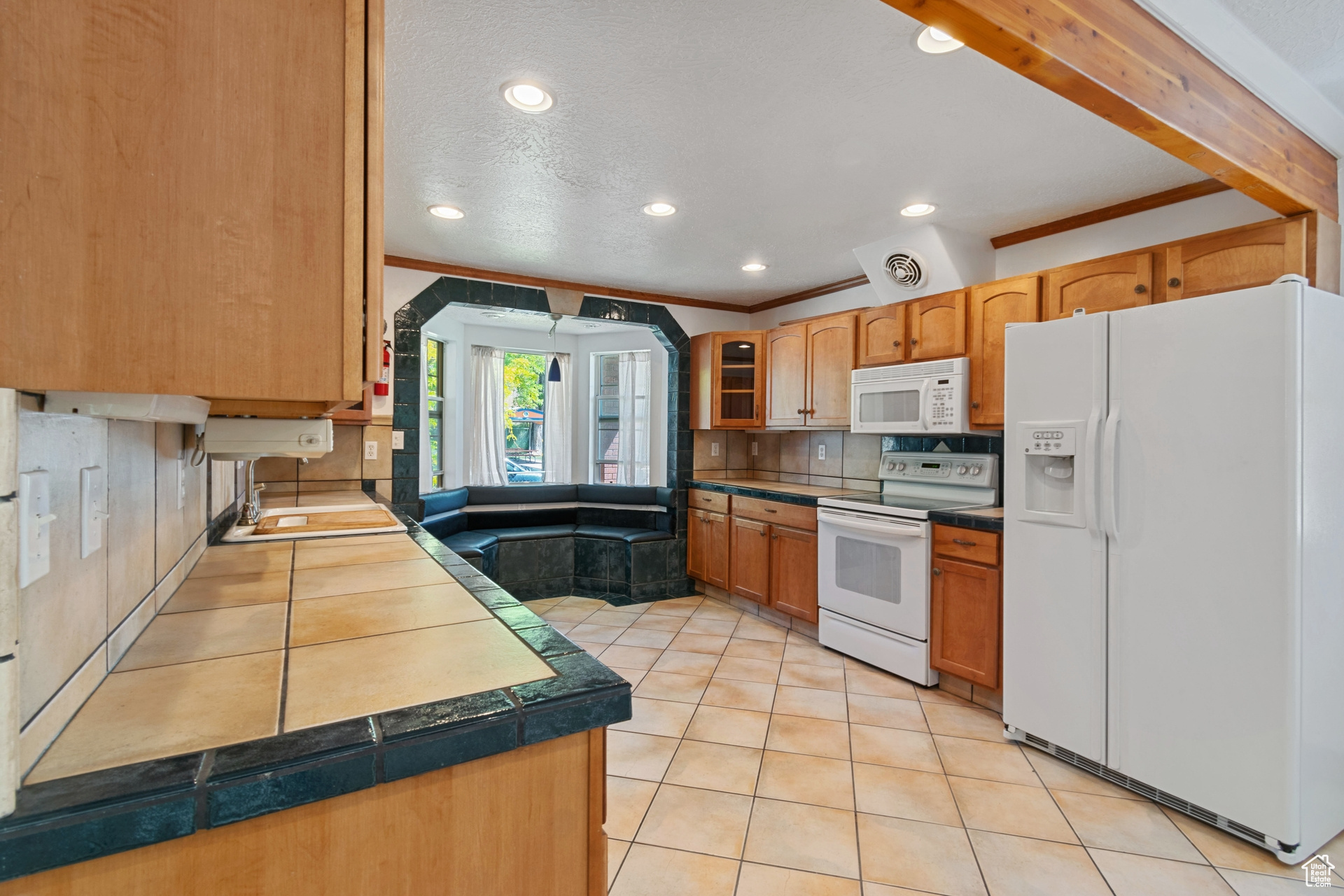 Kitchen featuring backsplash, white appliances, light tile floors, and crown molding