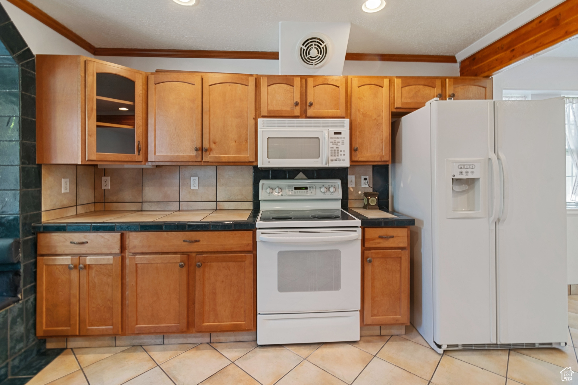 Kitchen featuring backsplash, crown molding, white appliances, and light tile floors