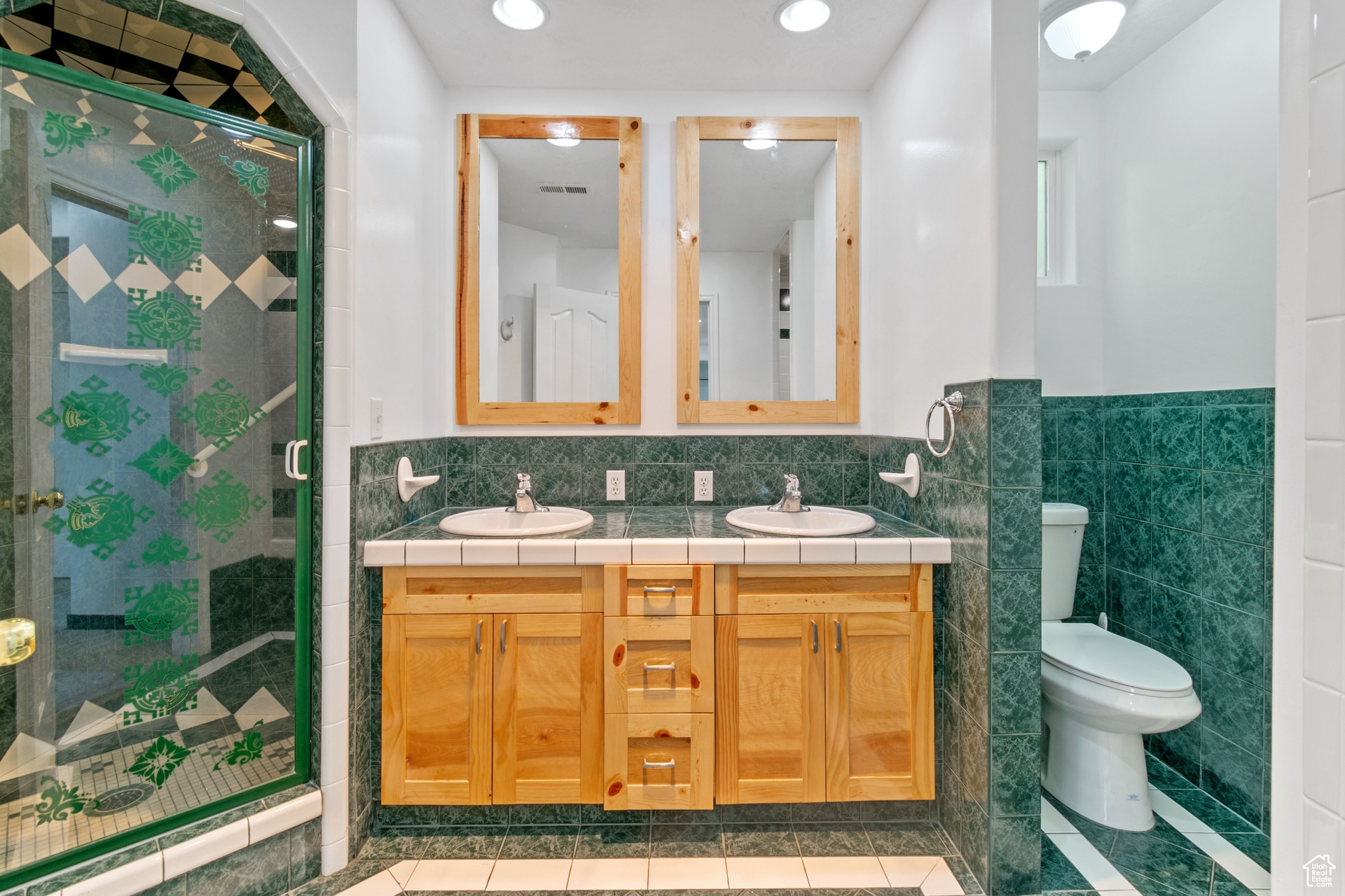 Bathroom featuring tile walls, toilet, tile floors, an enclosed shower, and double sink