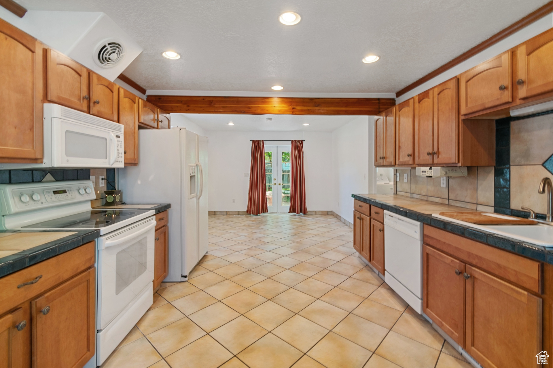 Kitchen with tile countertops, white appliances, and light tile flooring