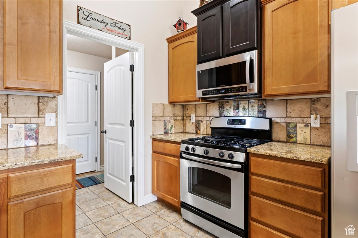 Kitchen featuring light stone countertops, backsplash, light tile floors, and stainless steel appliances