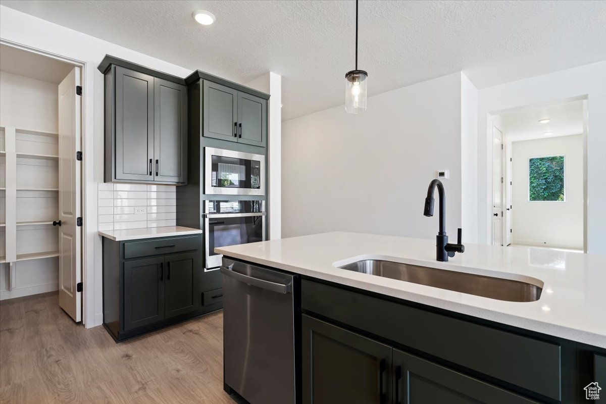 Kitchen featuring appliances with stainless steel finishes, light hardwood / wood-style flooring, sink, pendant lighting, and backsplash