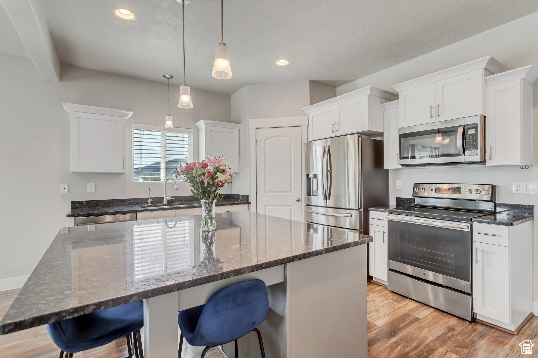 Kitchen featuring light hardwood / wood-style floors, hanging light fixtures, white cabinetry, a kitchen island, and appliances with stainless steel finishes