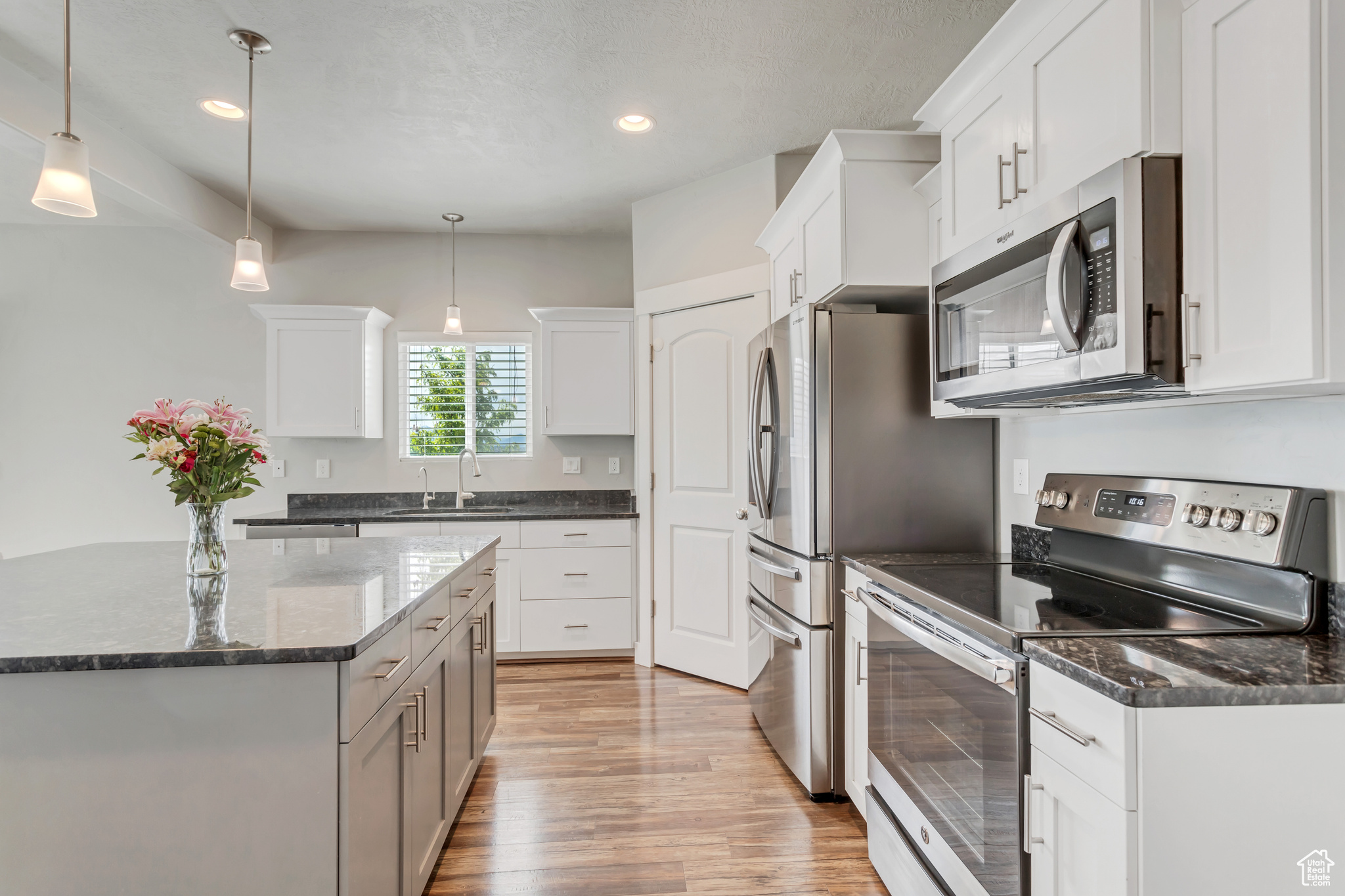 Kitchen featuring light wood-type flooring, appliances with stainless steel finishes, white cabinets, pendant lighting, and sink